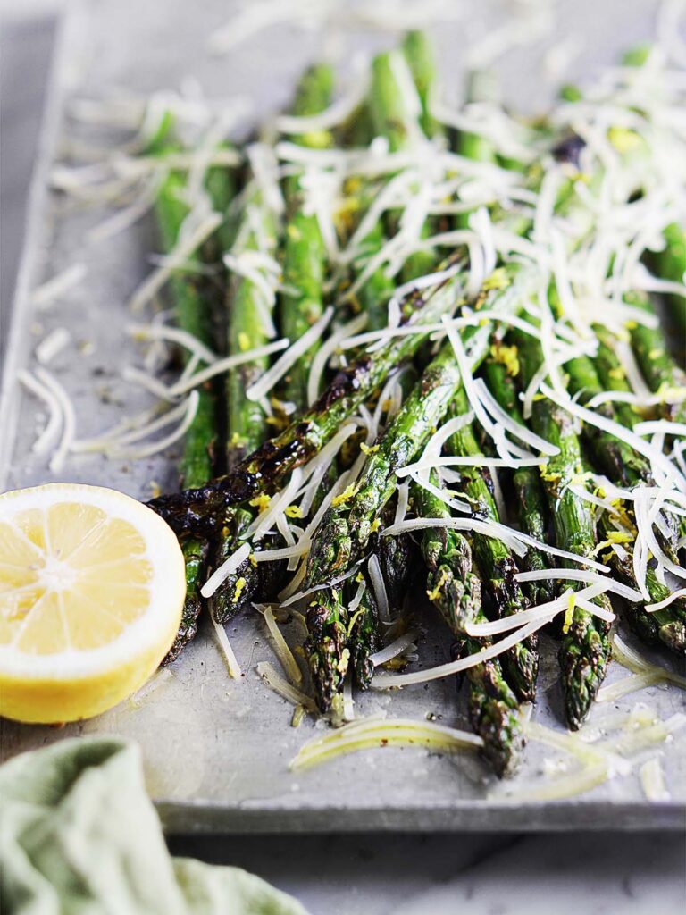 Asparagus on a tray topped with lemon zest and shredded parmesan.