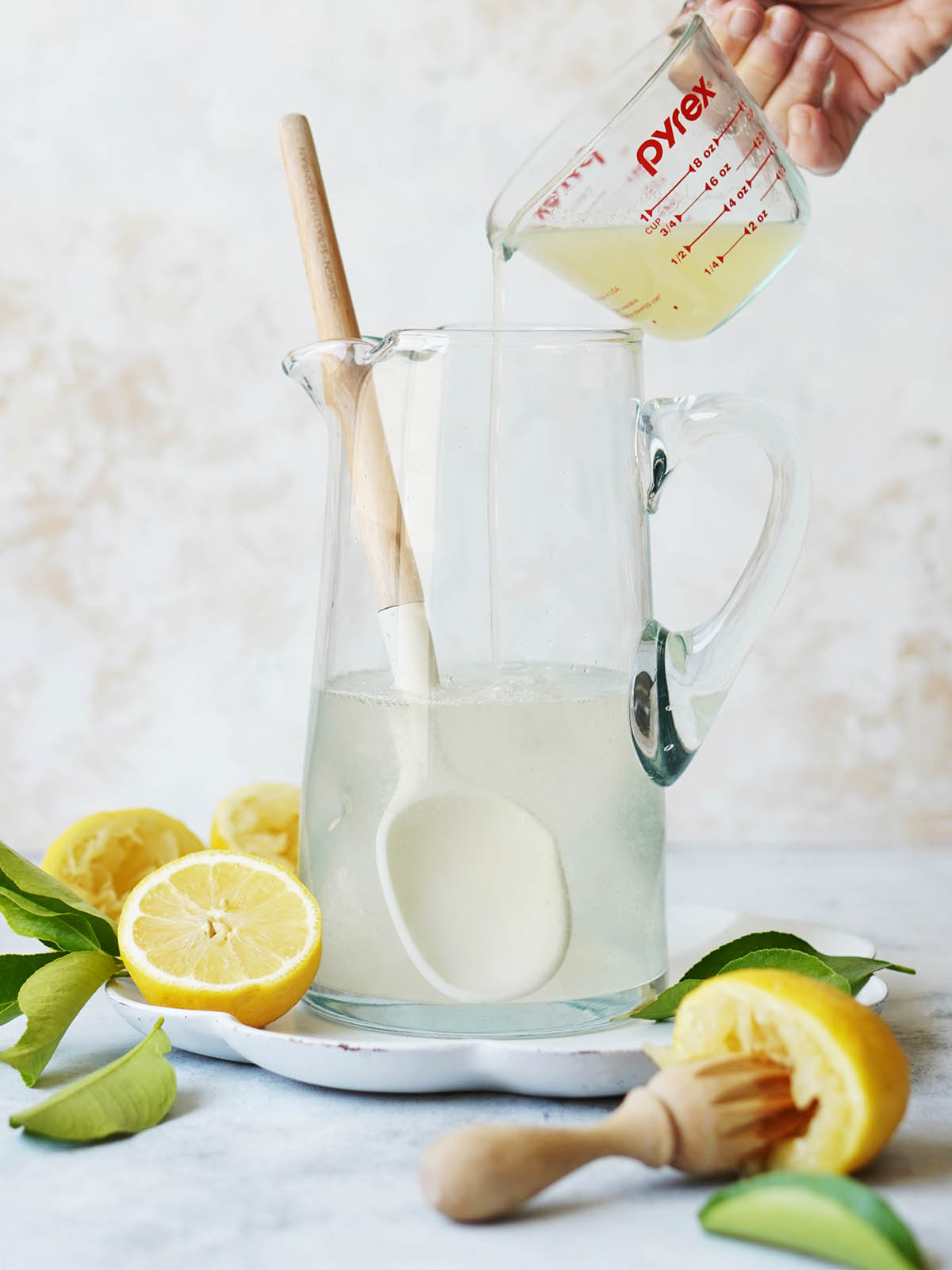A hand pouring lemon juice from a cup into a jar with water.