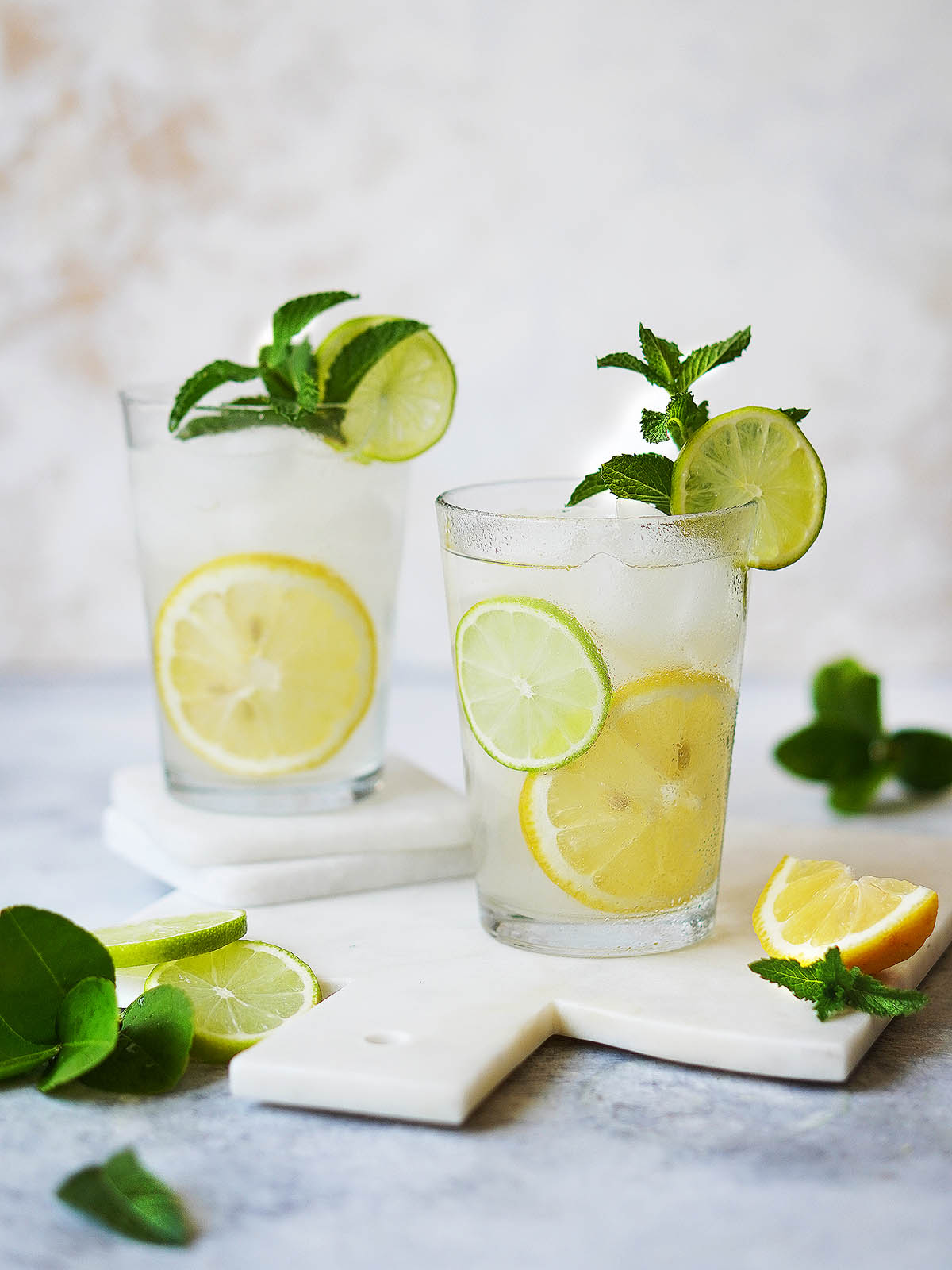 Two glasses filled with ice and lemonade garnished with lemons.