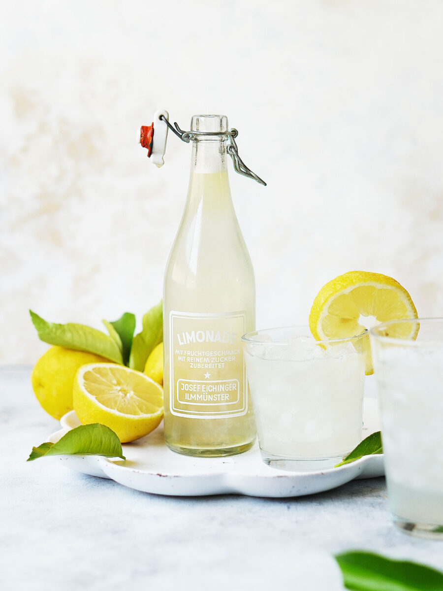 A jar of lemonade with fresh lemons on the side placed on a white tray.