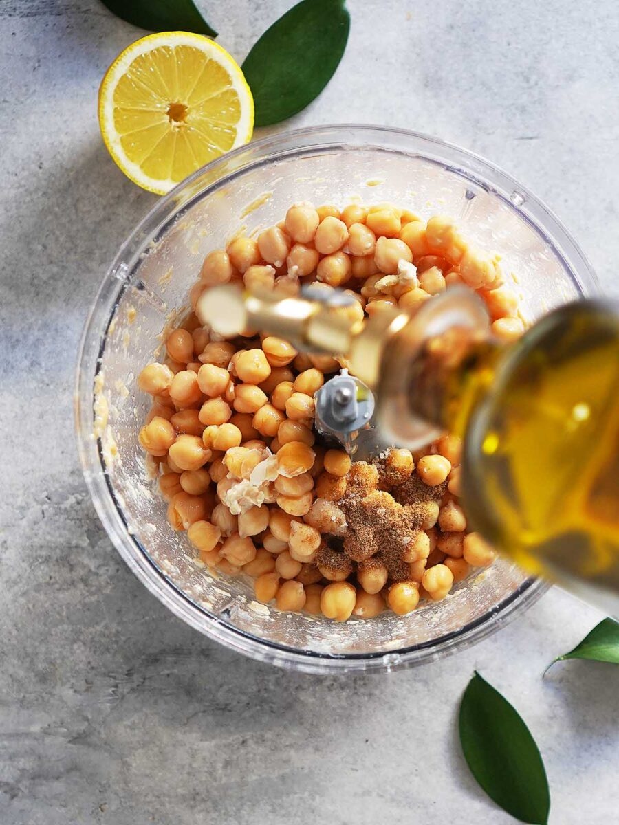 Adding oil to a food processor container with chickpeas.