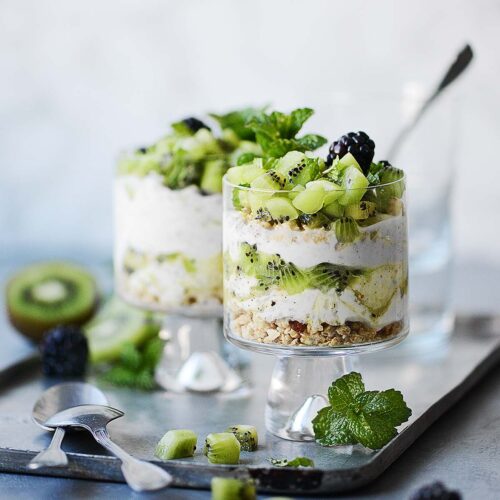 Two cute glasses with parfait topped with fresh kiwi placed on a metal tray.