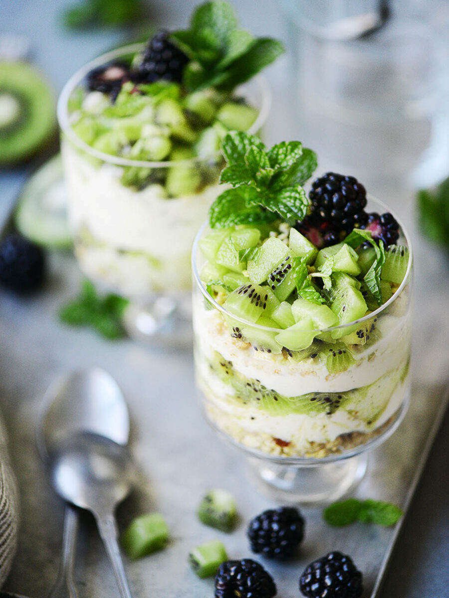 Two cute glasses with parfait topped with fresh kiwi placed on a metal tray.