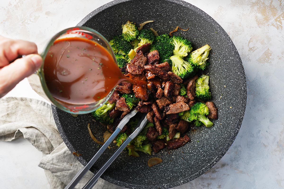 Adding asian sauce on cooked broccoli, onions and garlic on a wok.