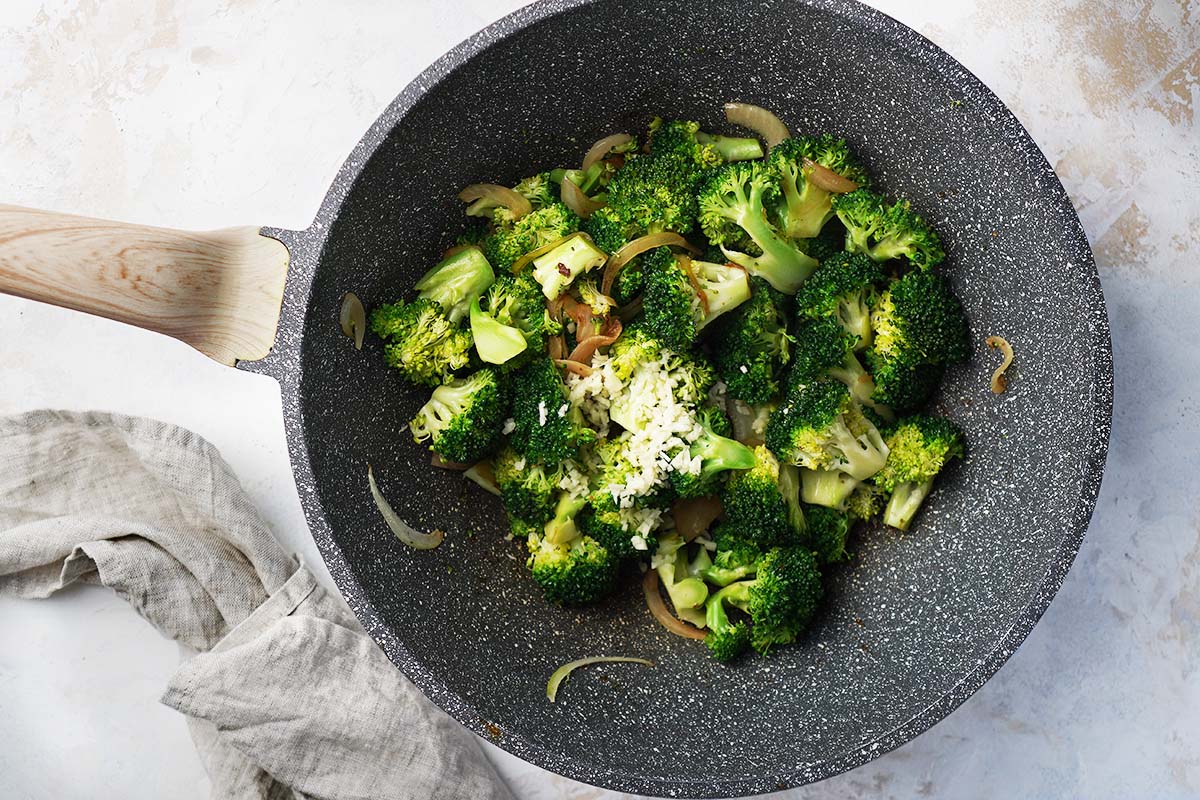 Cooking broccoli, onions and garlic on a wok.