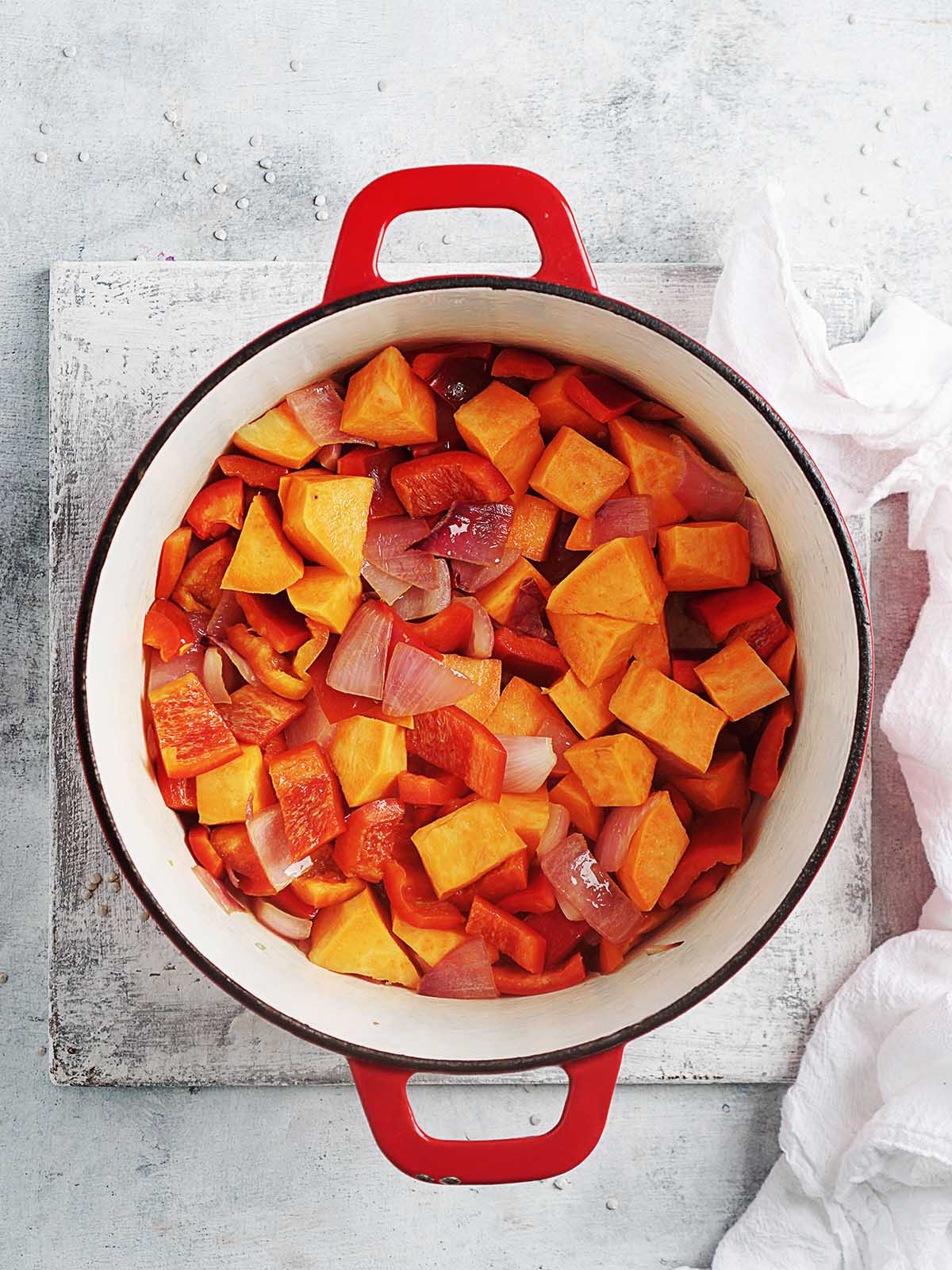 Sauteing pumpkin, sweet potato and red pepper in a large pot.