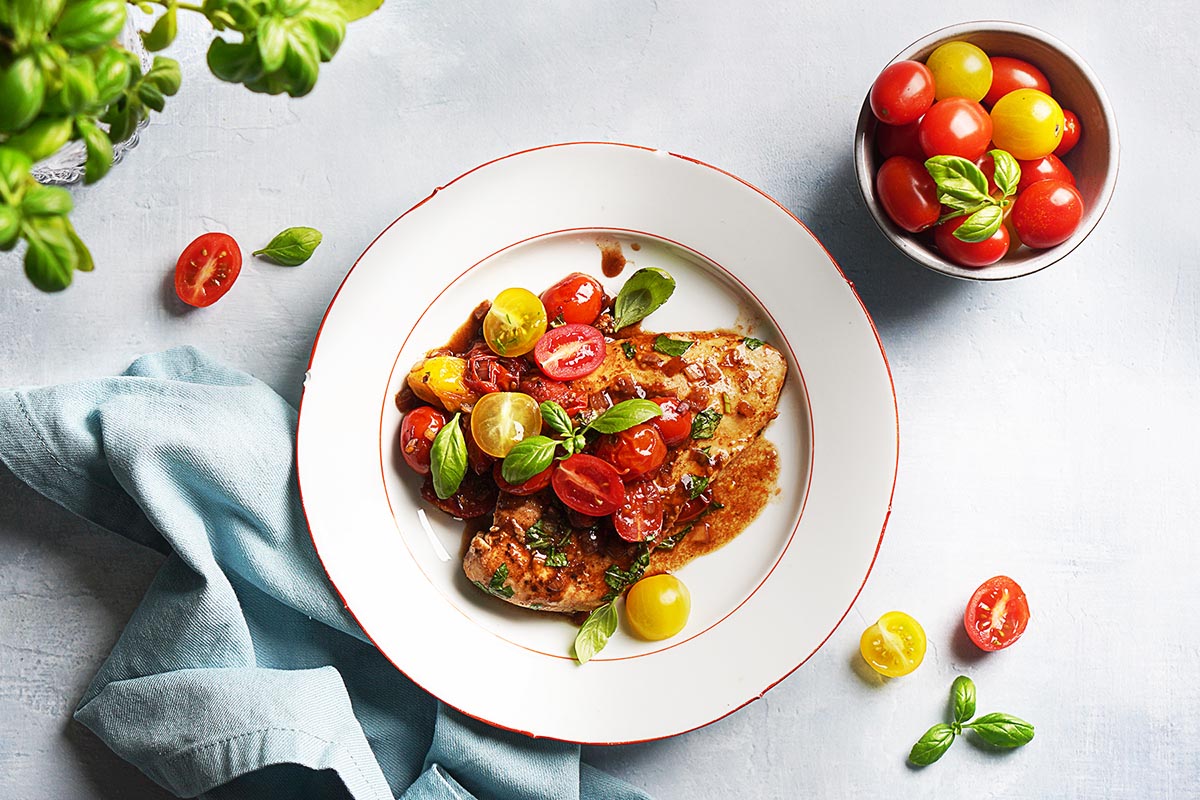 A white plate with chicken breast topped with balsamic tomatoes.