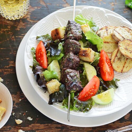 A plate with grilled steak and potatoes over a salad.