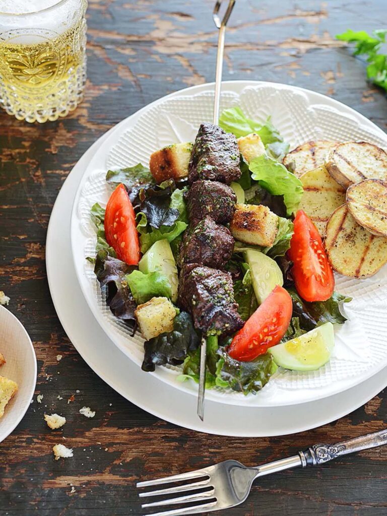 A plate with grilled steak and potatoes over a salad.